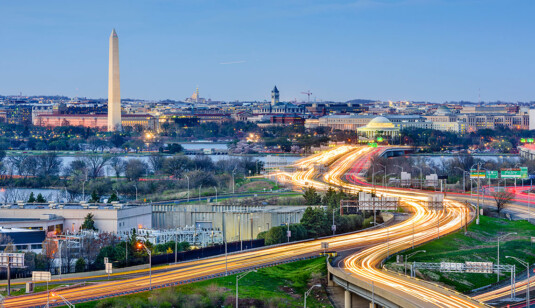 Wide shot of Washington DC during the evening featuring highways, lakes, and monuments